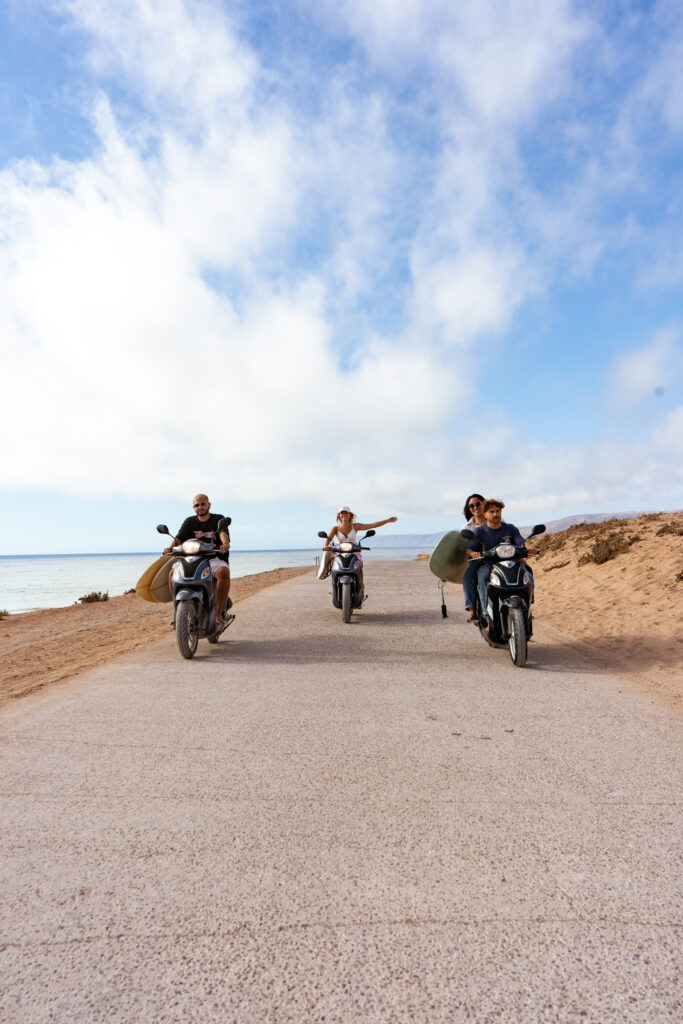  Customers driving scooters along the beach with surfboards